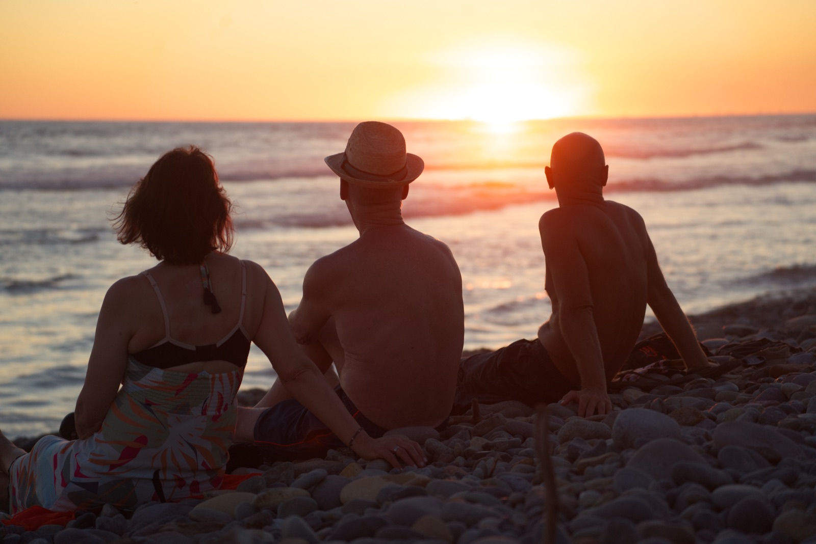 Drei Menschen sitzen am Strand und schauen in den Sonnenuntergang